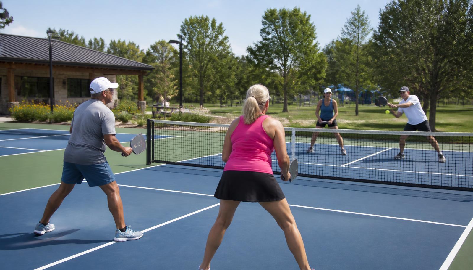Four adults playing doubles on municipal pickleball courts in a public park